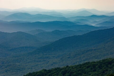 Layers of forested mountain ridges fade from green to pale blue into the hazy distance, seen from Look Rock Tower on the Foothills Parkway, Great Smoky Mountains, Tennessee.