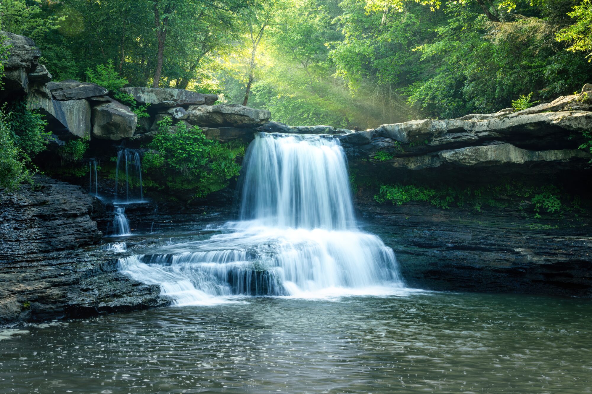 A backcountry waterfall in East Tennessee photographed as a long exposure, light filtering through the trees above.